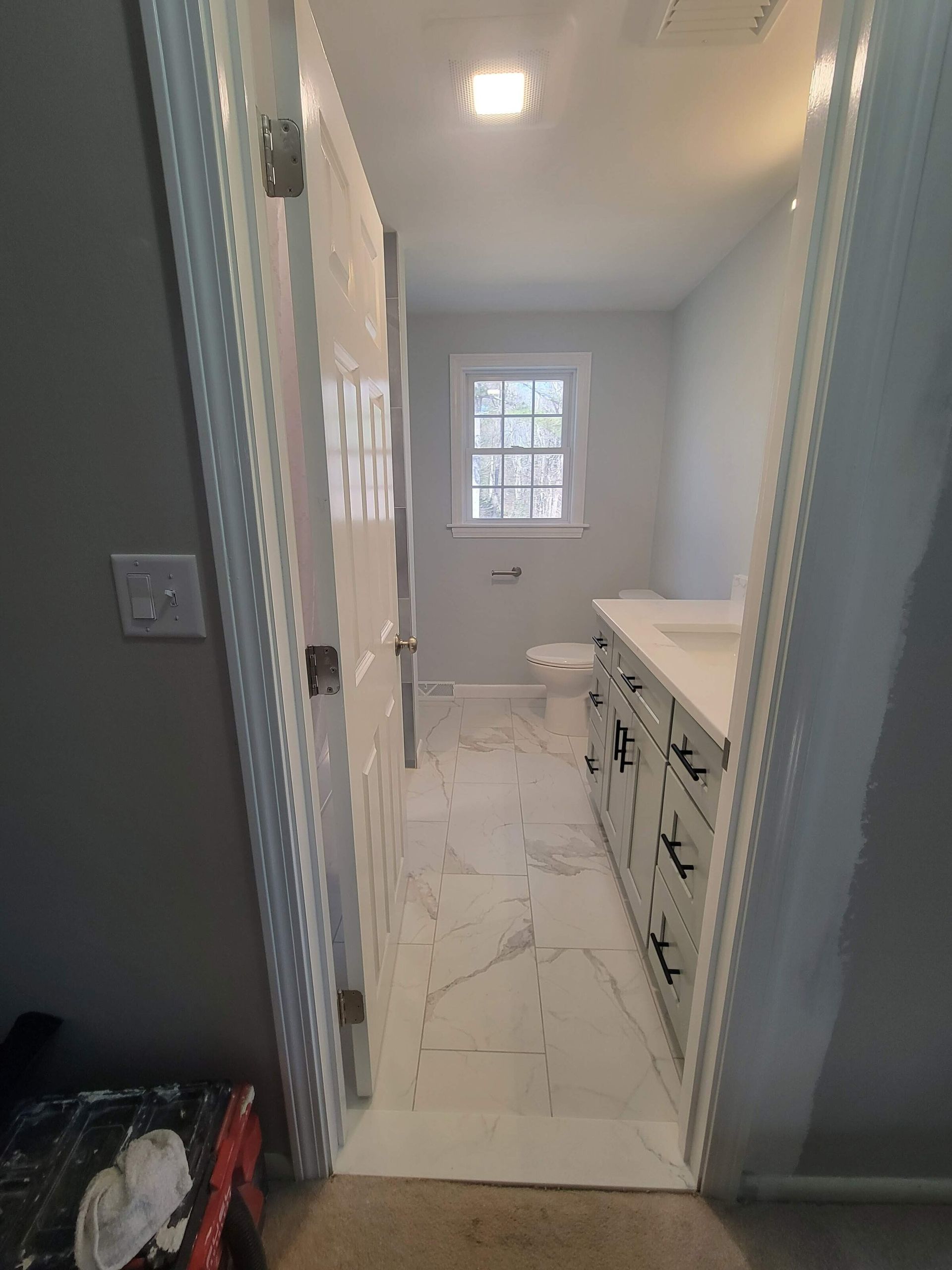 Bathroom interior with white tile floors, a vanity, toilet, and a window.