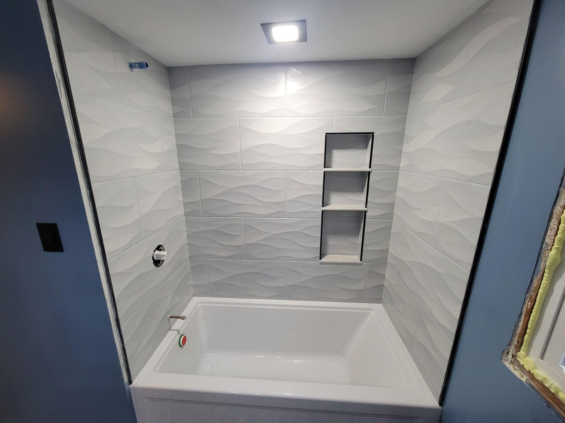 A renovated bathroom with a white tub, gray wave-patterned tile, and built-in shelving.