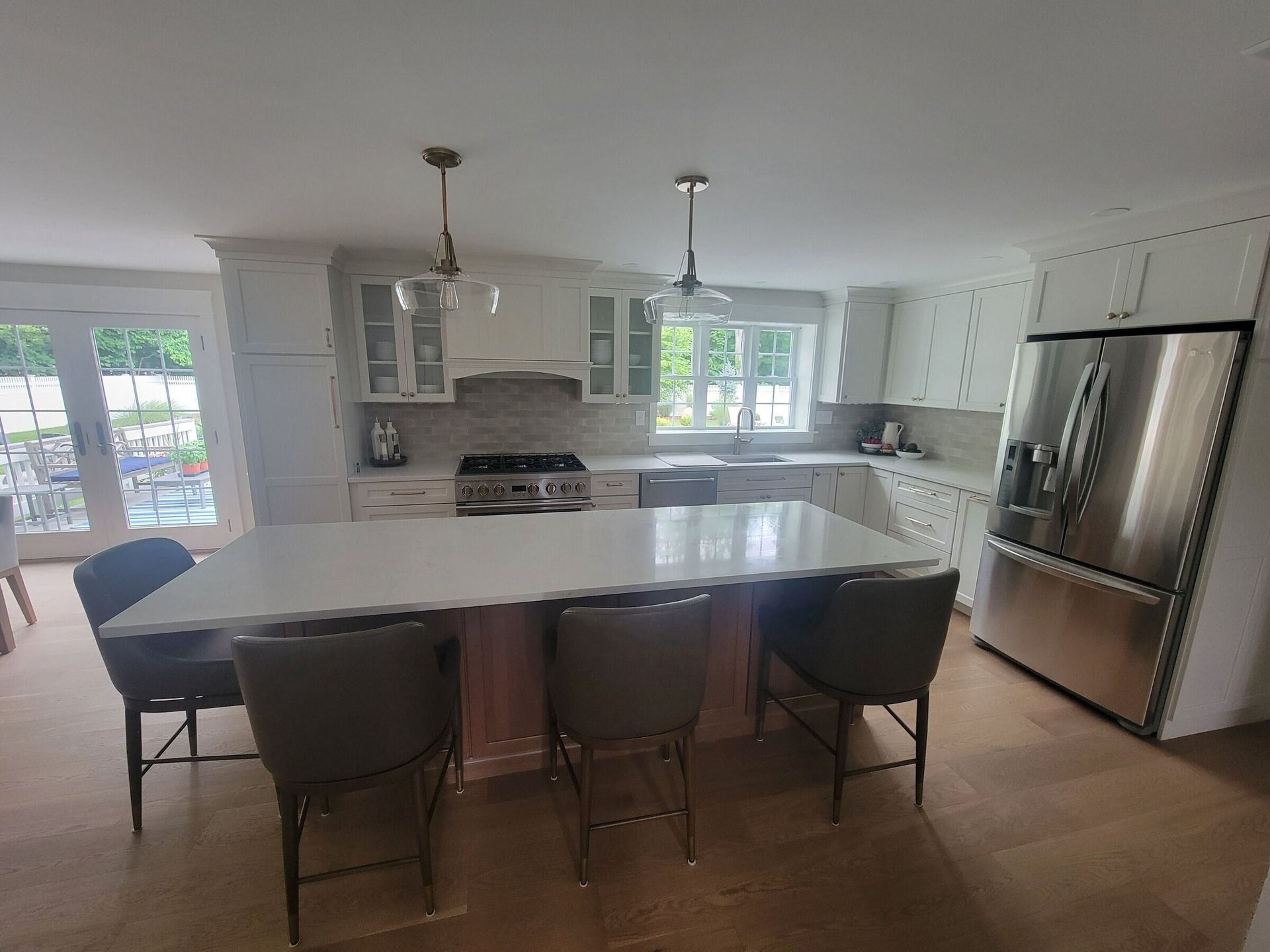 Modern kitchen with white cabinets, island with seating, stainless steel fridge, and pendant lights.