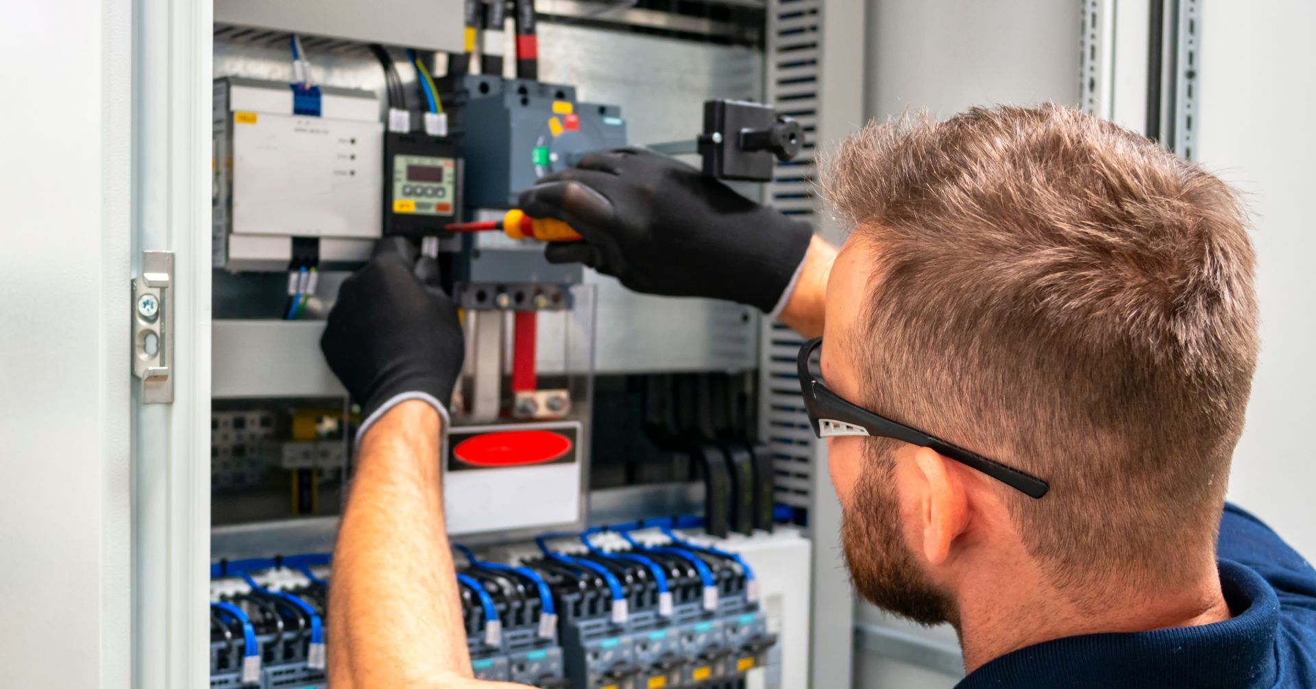 A man is working on an electrical box with a screwdriver.