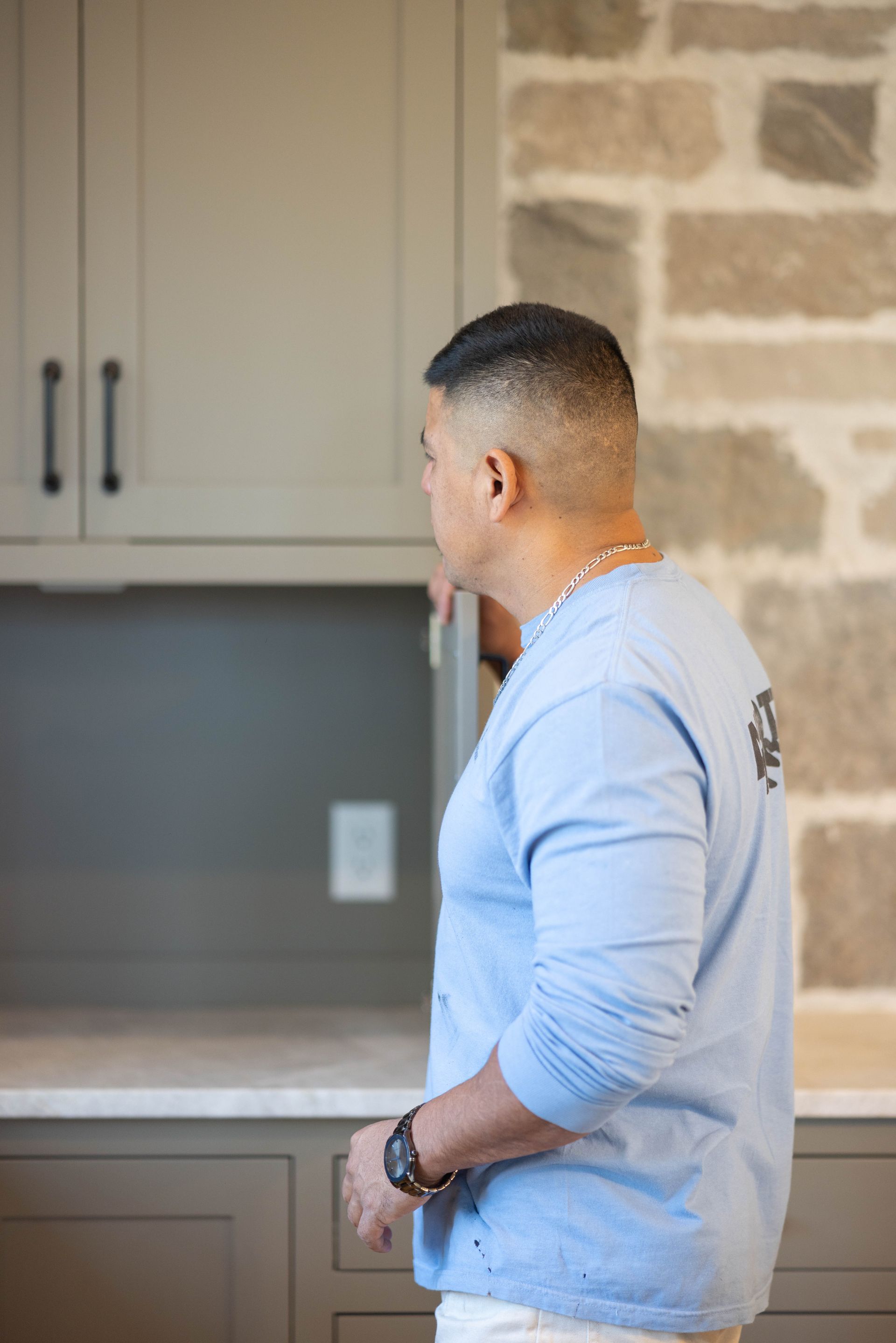 A man in a blue shirt is standing in front of a refrigerator in a kitchen.
