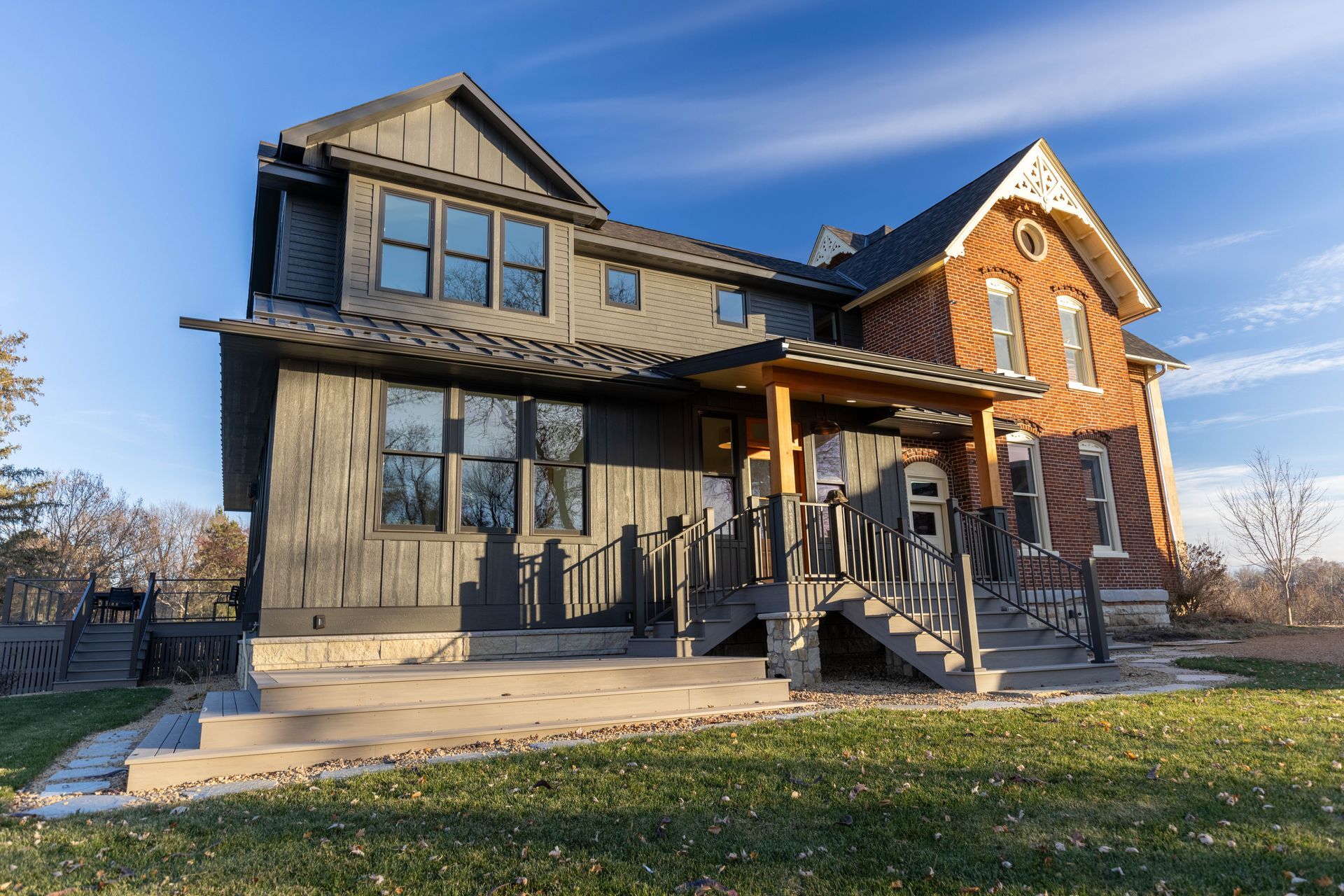 A large brick house with a porch and stairs is sitting on top of a lush green field.
