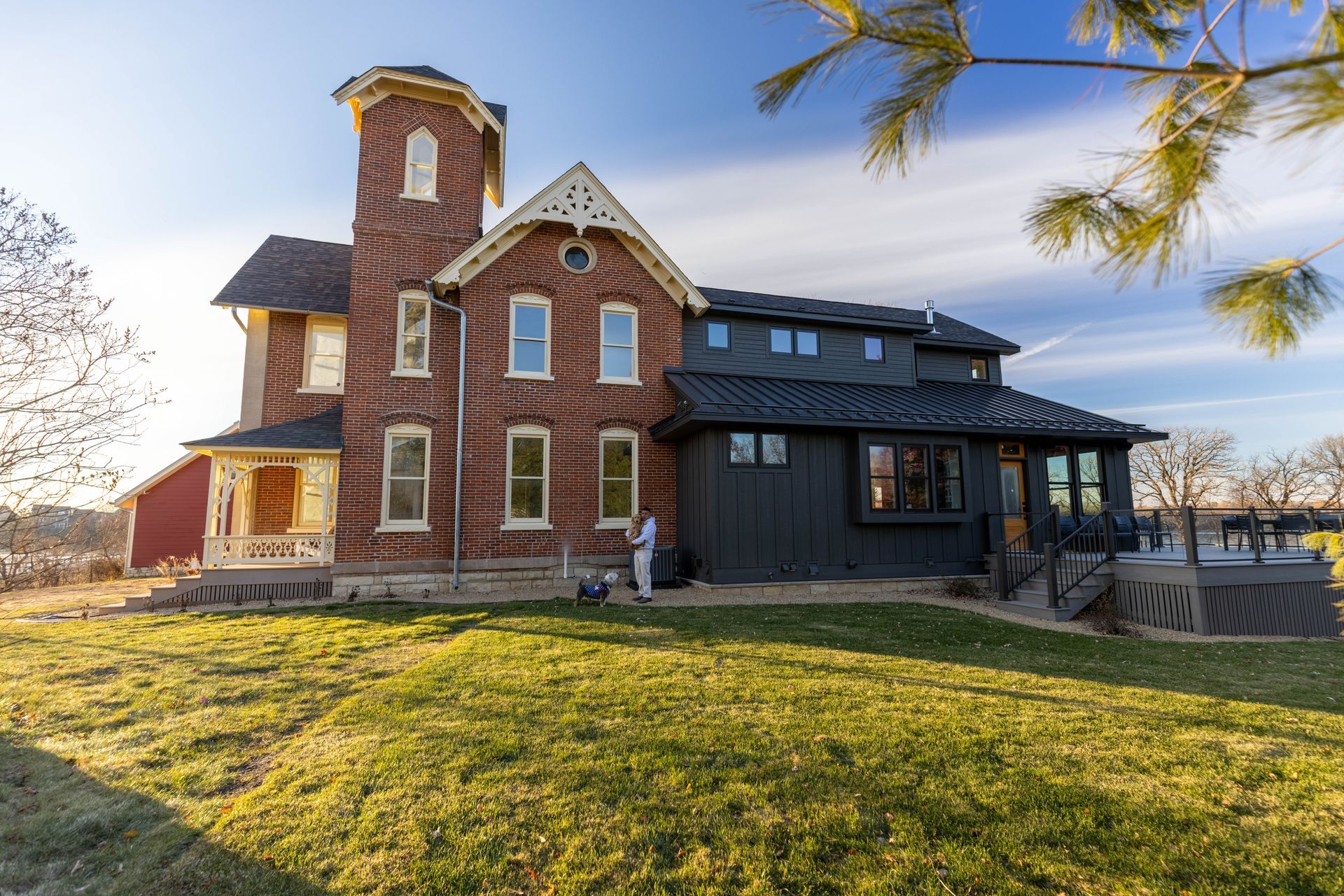 A large brick house with a black roof is sitting on top of a lush green field.