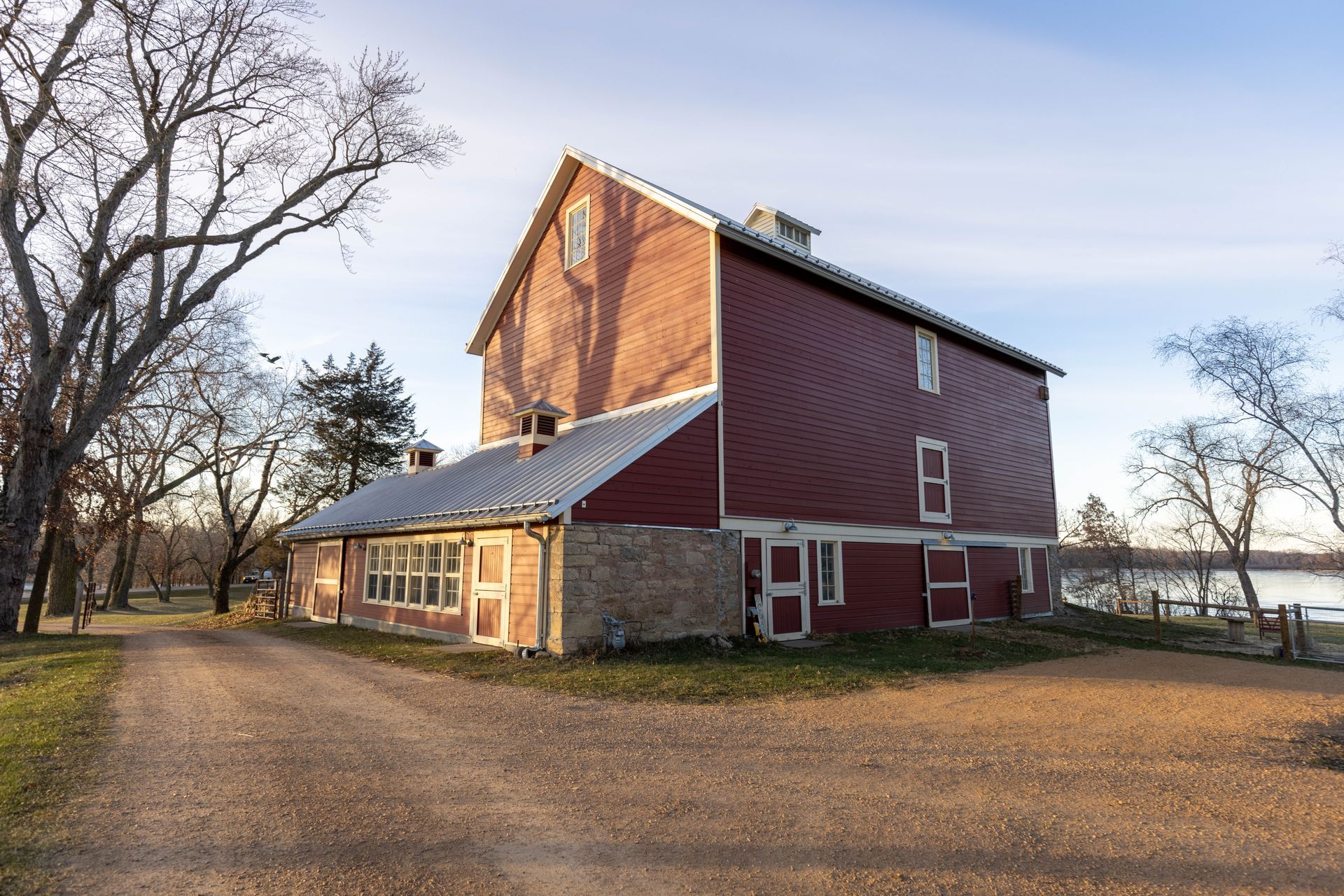 A large red barn is sitting on top of a dirt road next to a lake.