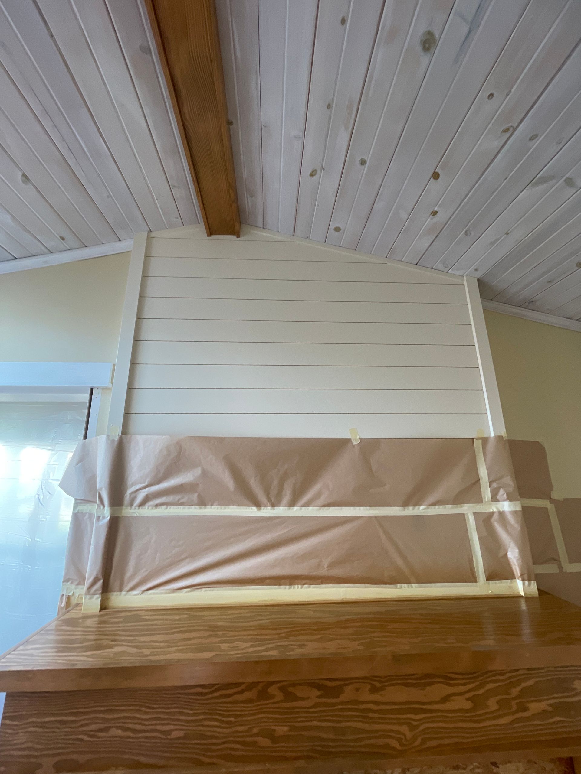 A wooden wall is being painted in a room with a wooden ceiling.