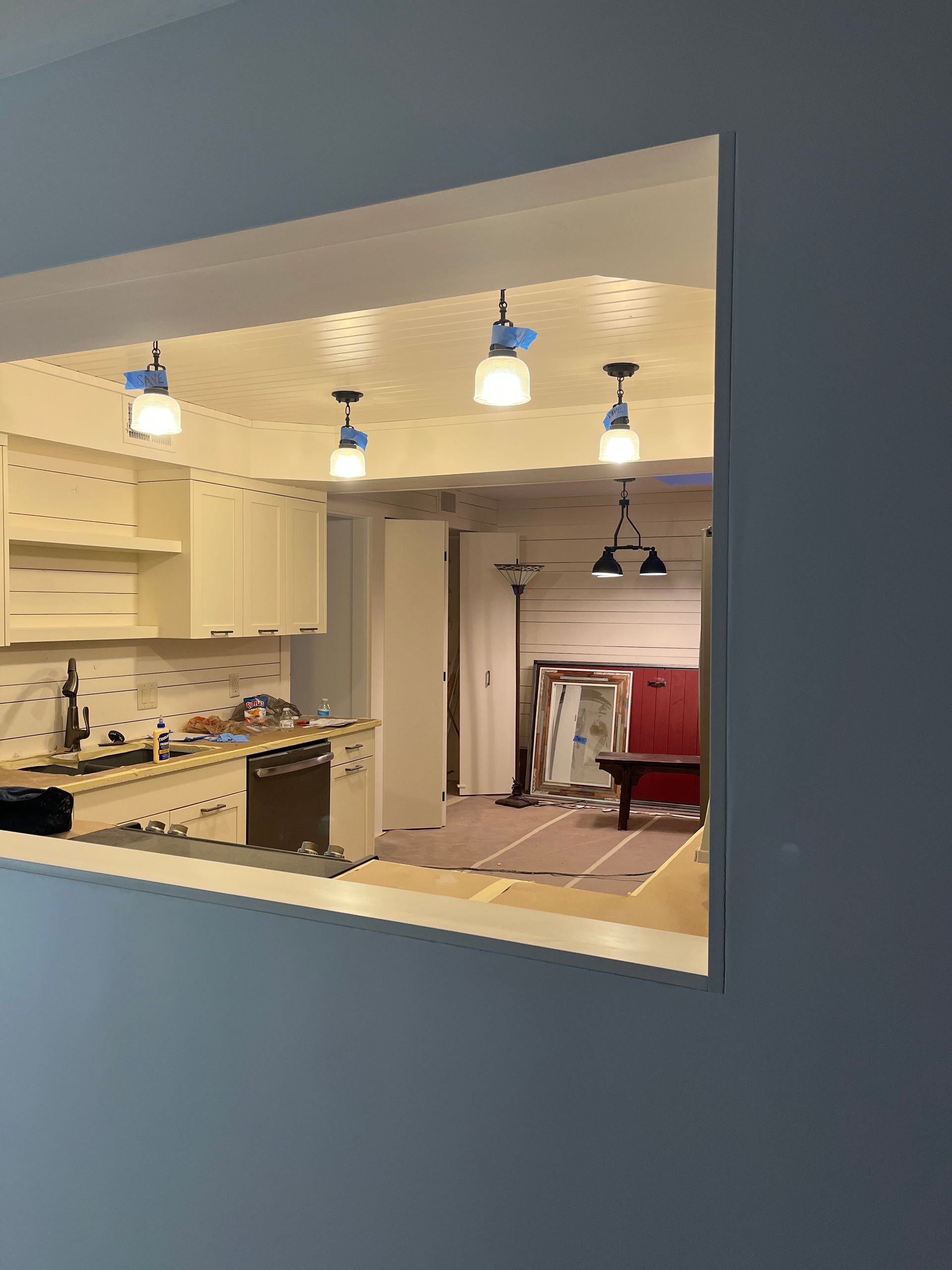 A kitchen is being remodeled and there is a window between the kitchen and the living room.