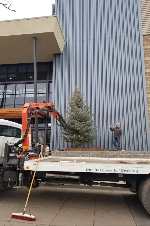 A tow truck with a broom attached to it is parked in front of a building.