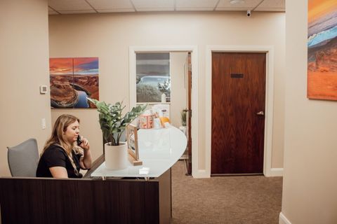 A woman is sitting at a desk in a lobby talking on a cell phone.