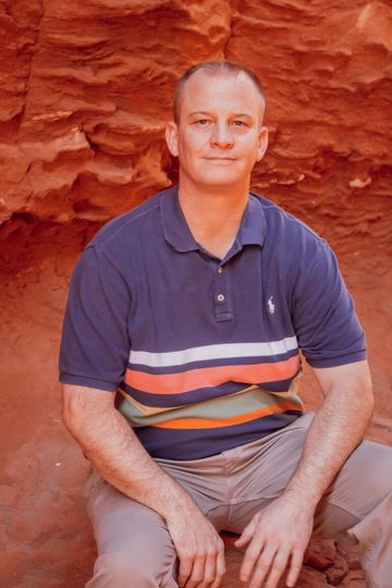 A man in a blue polo shirt is sitting on a rock