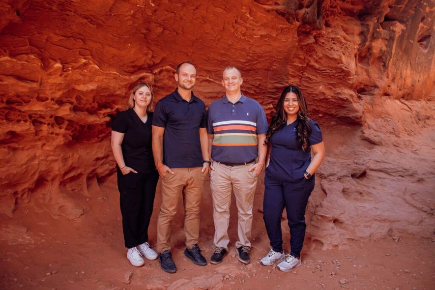 A group of people are posing for a picture in front of a red rock formation.