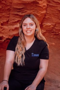 A woman in a black shirt is sitting in front of a red rock wall.