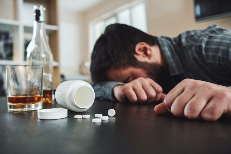 A man is laying on a table with a bottle of alcohol and pills.