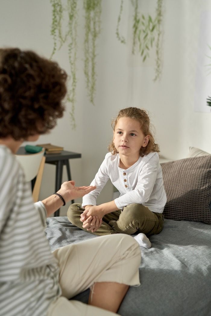 A woman is talking to a little girl who is sitting on a bed.