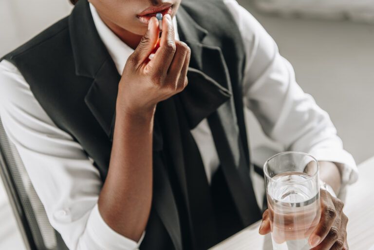 A woman is taking a pill and drinking a glass of water.