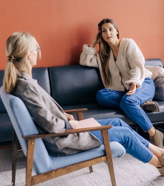 Two women are sitting on a couch talking to each other.