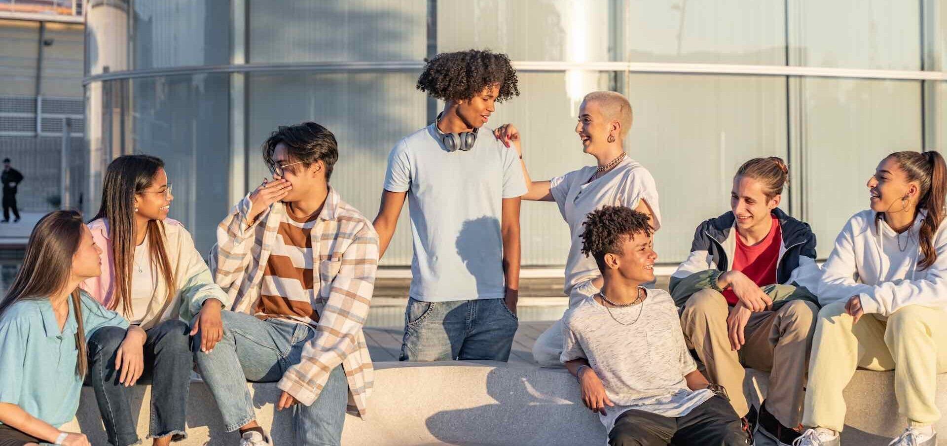 A group of young people are sitting on a bench in front of a building.