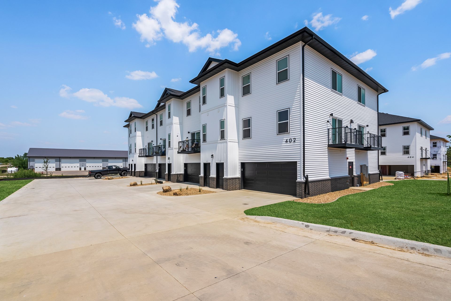 A three-story white apartment building with black trim and garage doors under a clear blue sky.