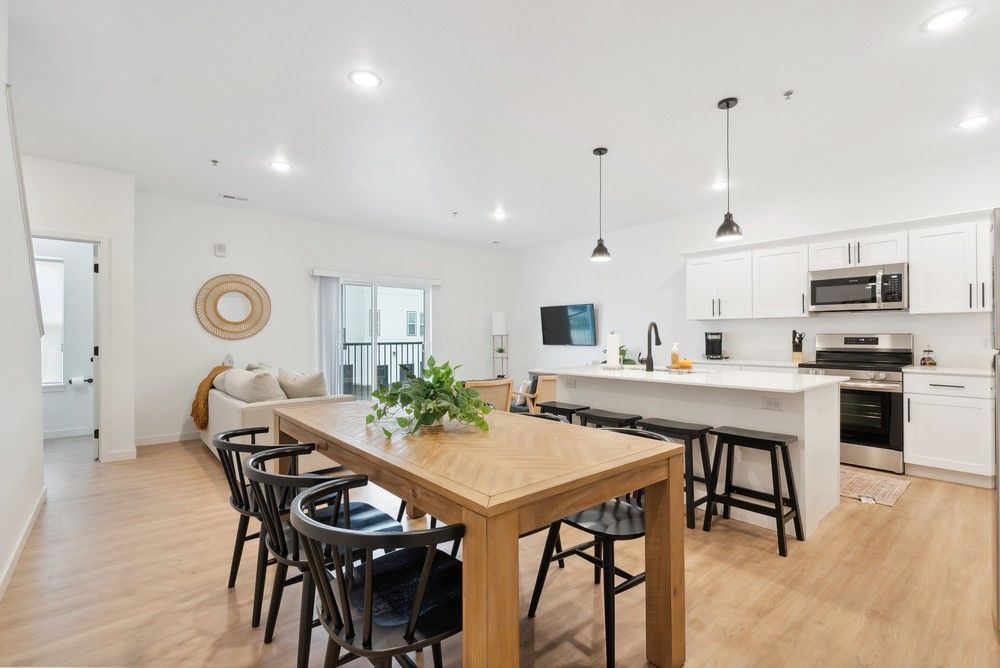 An open-concept room features a wooden dining table, a kitchen island with stools, and white cabinetry.