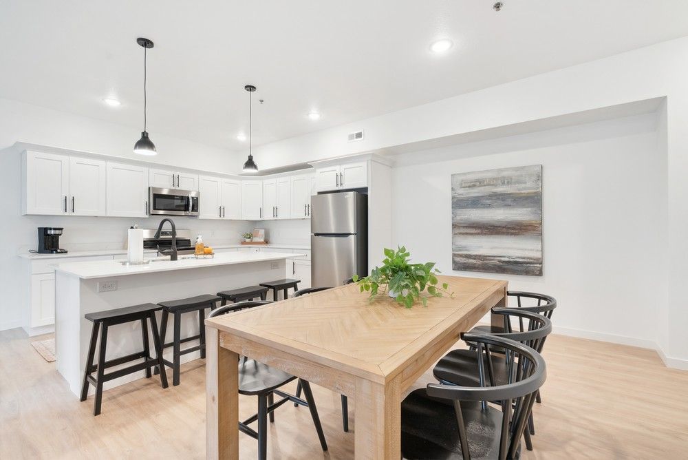 Modern kitchen with white cabinets, stainless steel appliances, a center island with stools, and a wooden dining table.