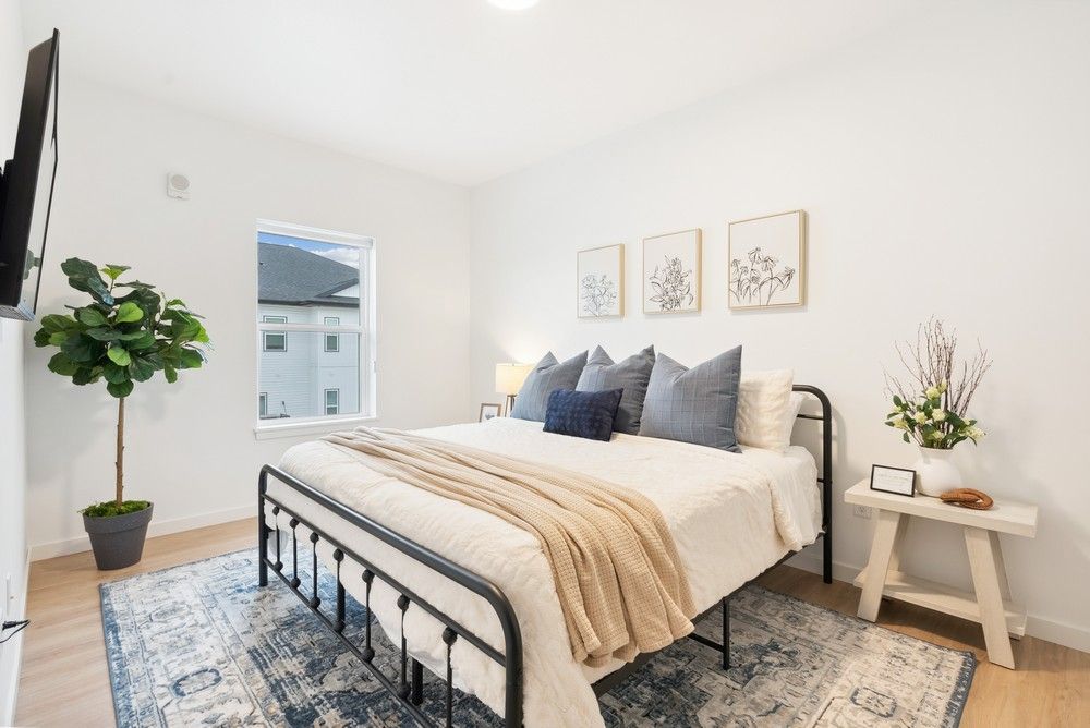 A modern bedroom with a black metal bed frame, cream bedding, a beige throw, blue pillows, and a patterned area rug.