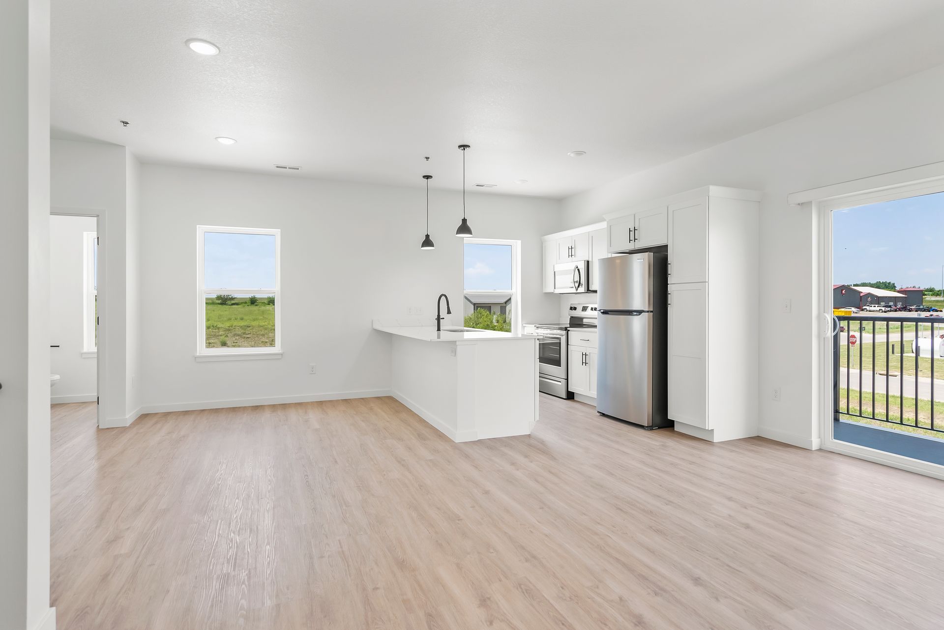 A bright, open-plan kitchen and living area featuring white cabinets, stainless steel appliances, and wood-look flooring.