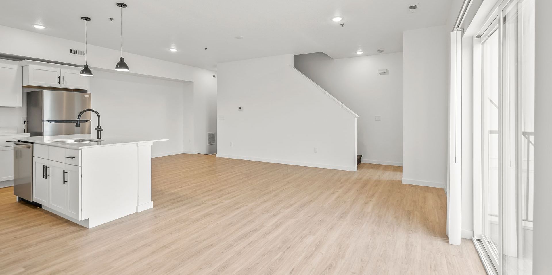 A bright, open-concept kitchen and living area featuring white cabinets, stainless appliances, and light wood flooring.