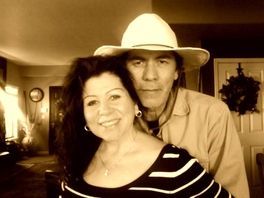 A man and a woman are posing for a picture in a living room . the woman is wearing a cowboy hat.