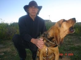 A man in a cowboy hat is kneeling next to a brown dog