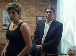 A man in a suit stands next to a woman in a black tank top