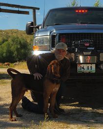 A man is kneeling down next to a dog in front of a truck.