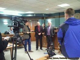 A man in a blue jacket is standing in front of a camera