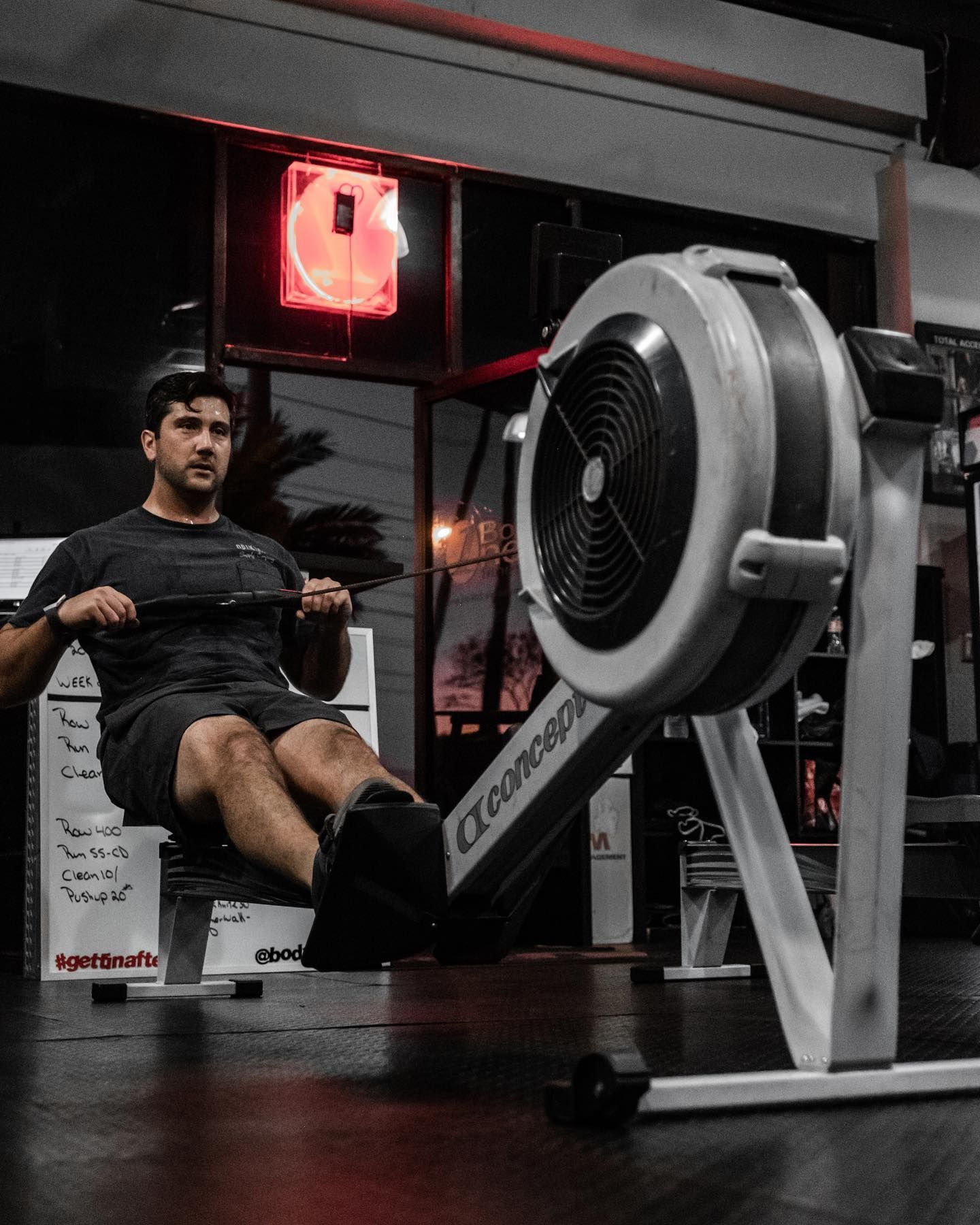 Woman in gym lifts kettlebell overhead, legs apart.