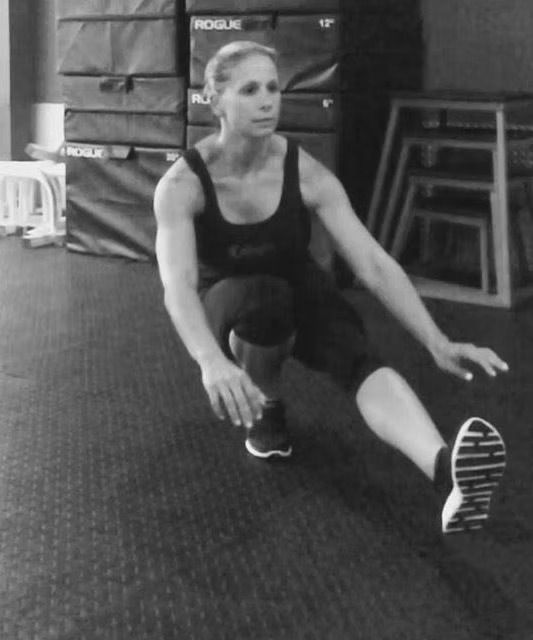 Woman doing a single-leg squat exercise in a gym. She reaches forward with arms.