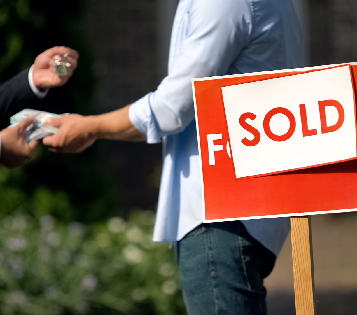 The agent and buyer swap cash and house keys beside a bright SOLD sign.