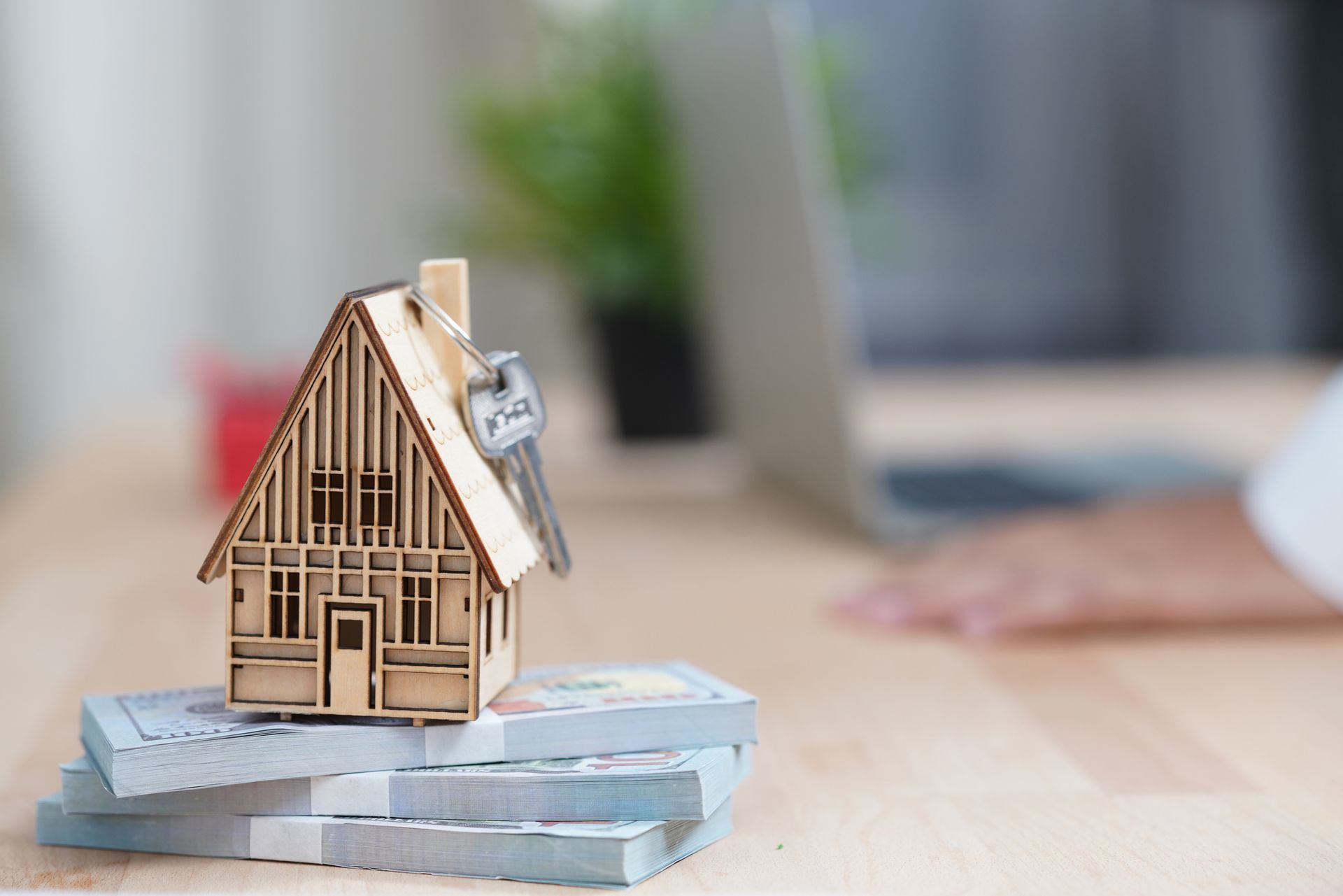 A wooden house model placed on a stack of money over a desk, highlighting quick home sale.