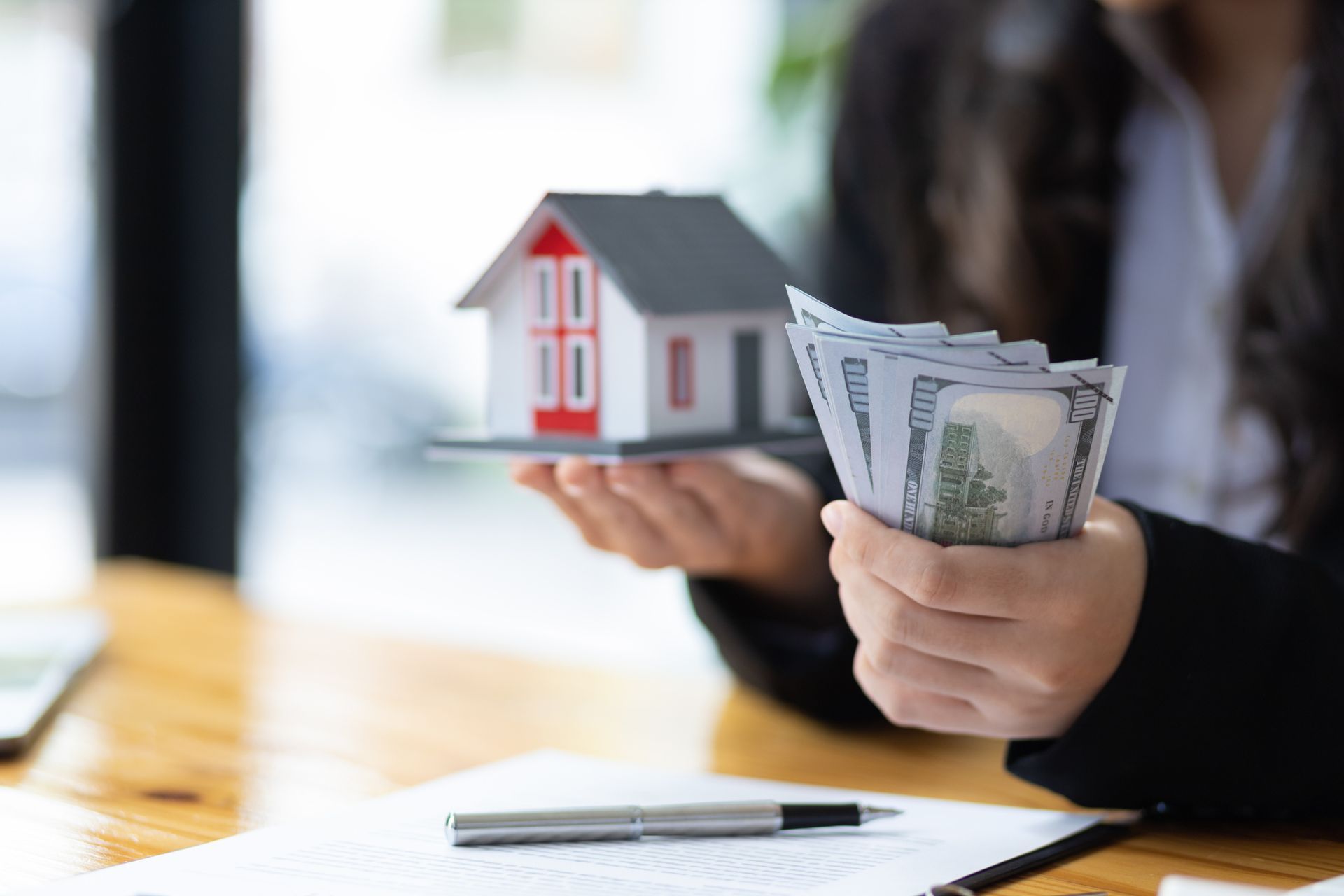 Home buyer holding cash and a mock-up home in her office. Home buyer holding cash and a mock-up home in her office.