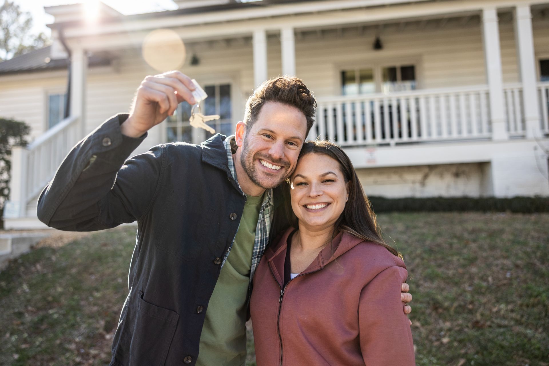 A young couple is holding house keys in front of their new home.