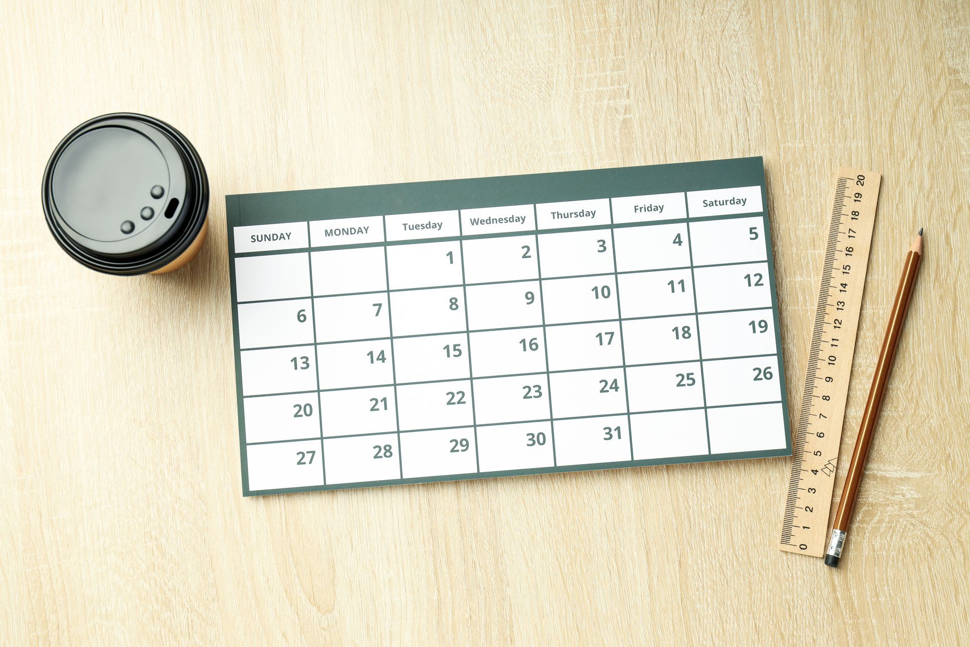 Calendar, coffee cup, ruler, and pencil on a light-colored surface.