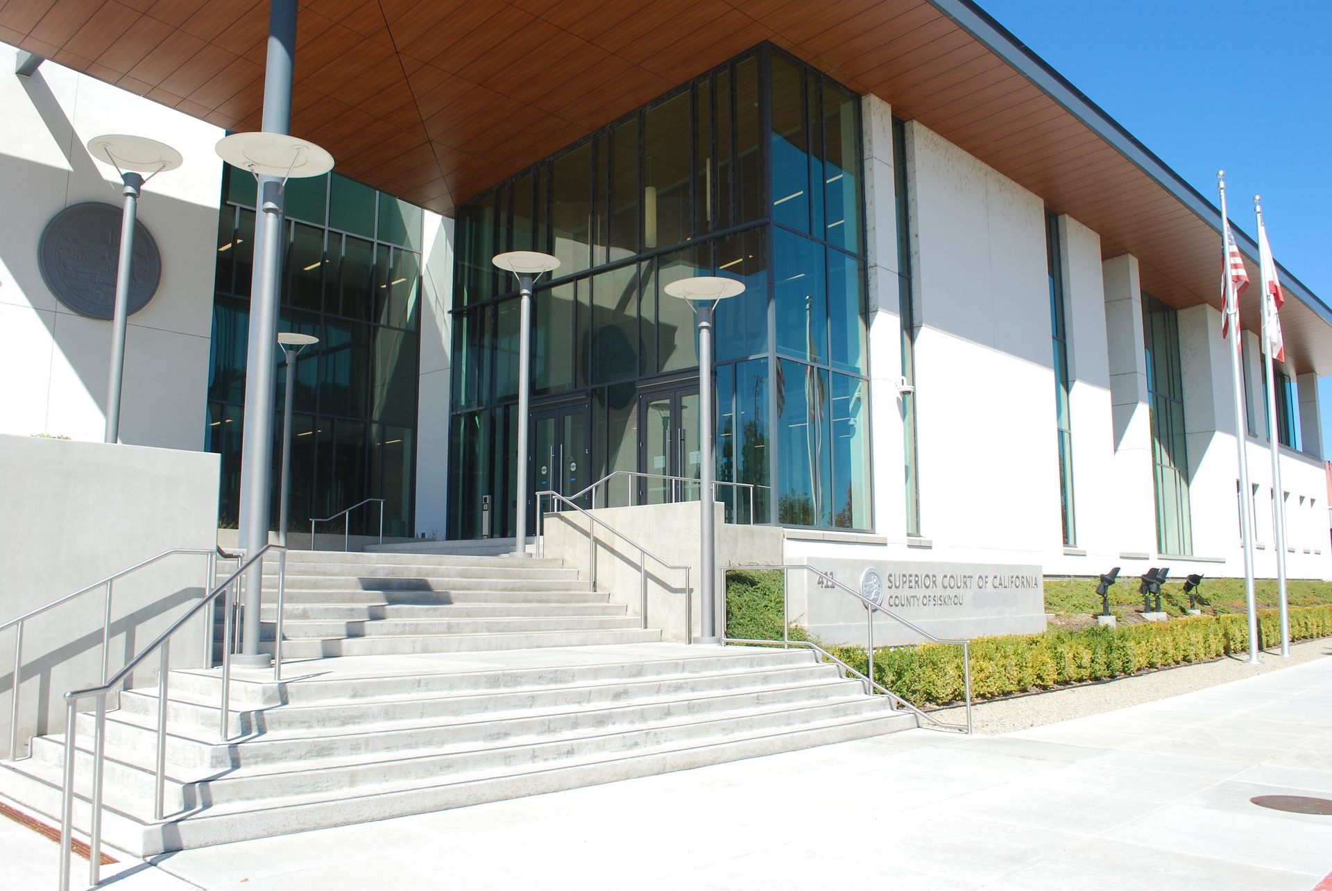 Modern building entrance with glass doors, concrete stairs, and light posts. 