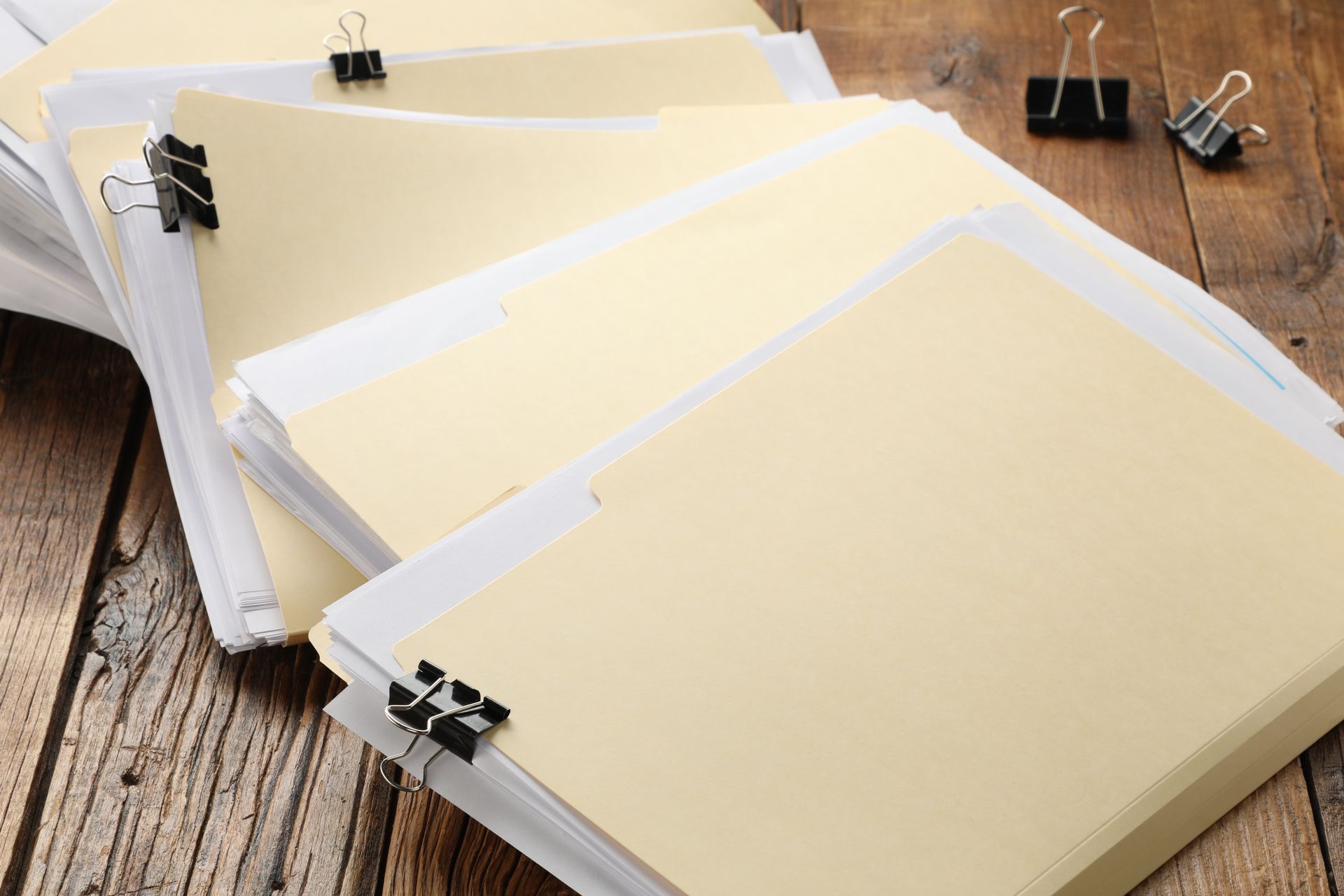 Piles of papers held together with binder clips on a wooden surface.