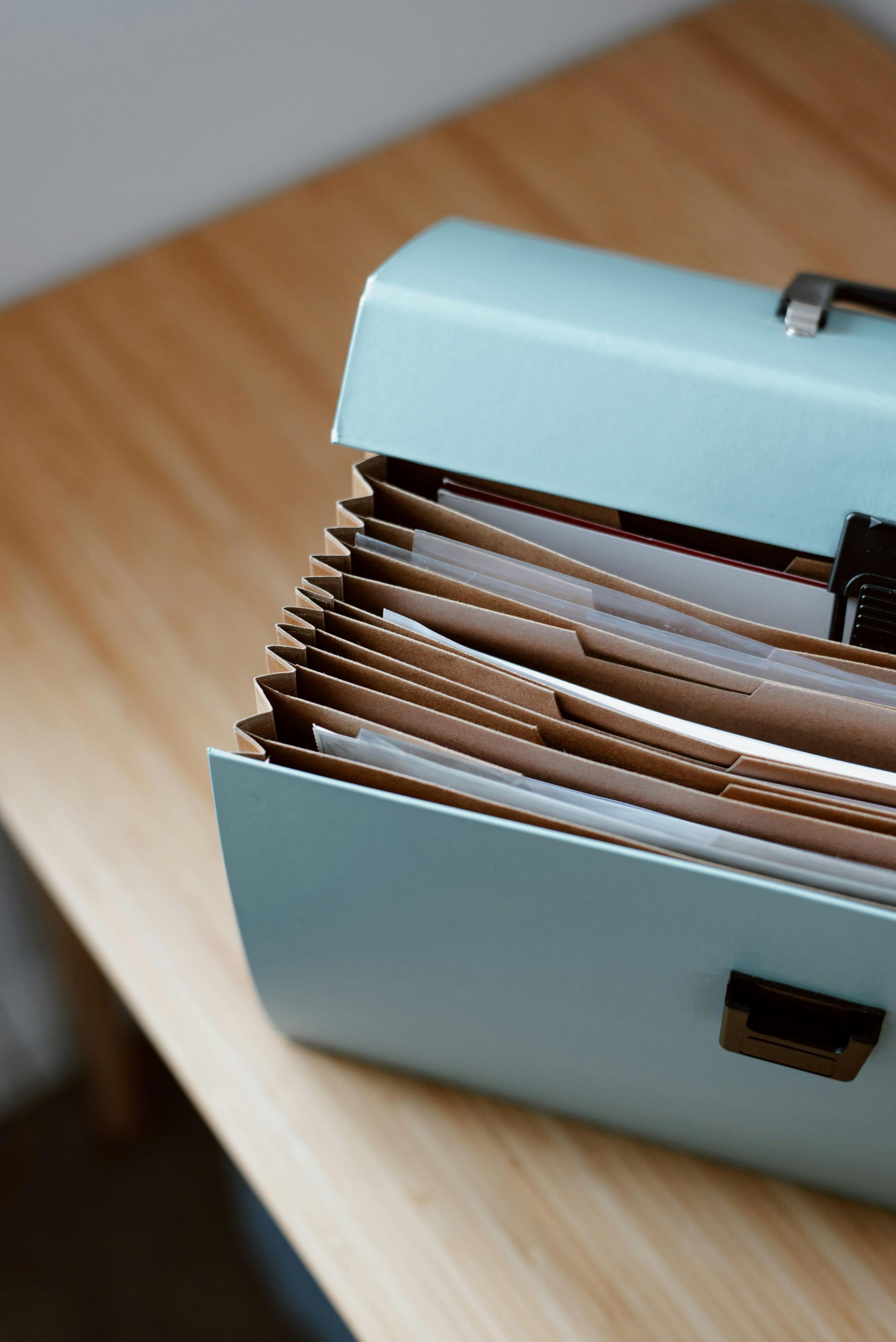 Blue accordion file on a light wood surface, filled with papers, partially open.