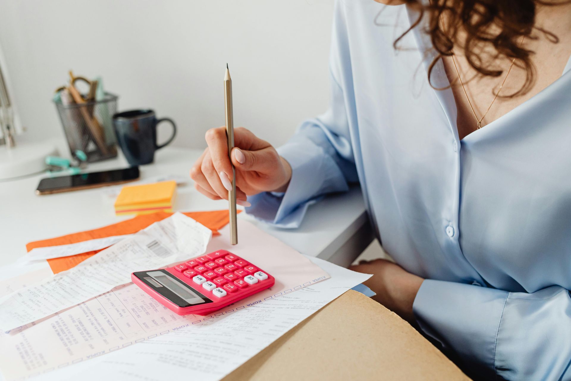 Person using a pink calculator on a desk with papers. A pencil is in hand.