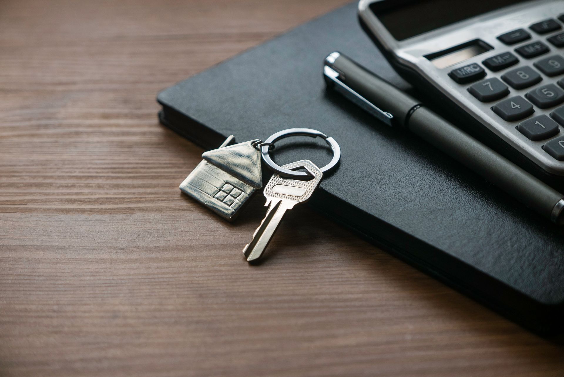 Keys with house charm, pen, and calculator on a notepad.