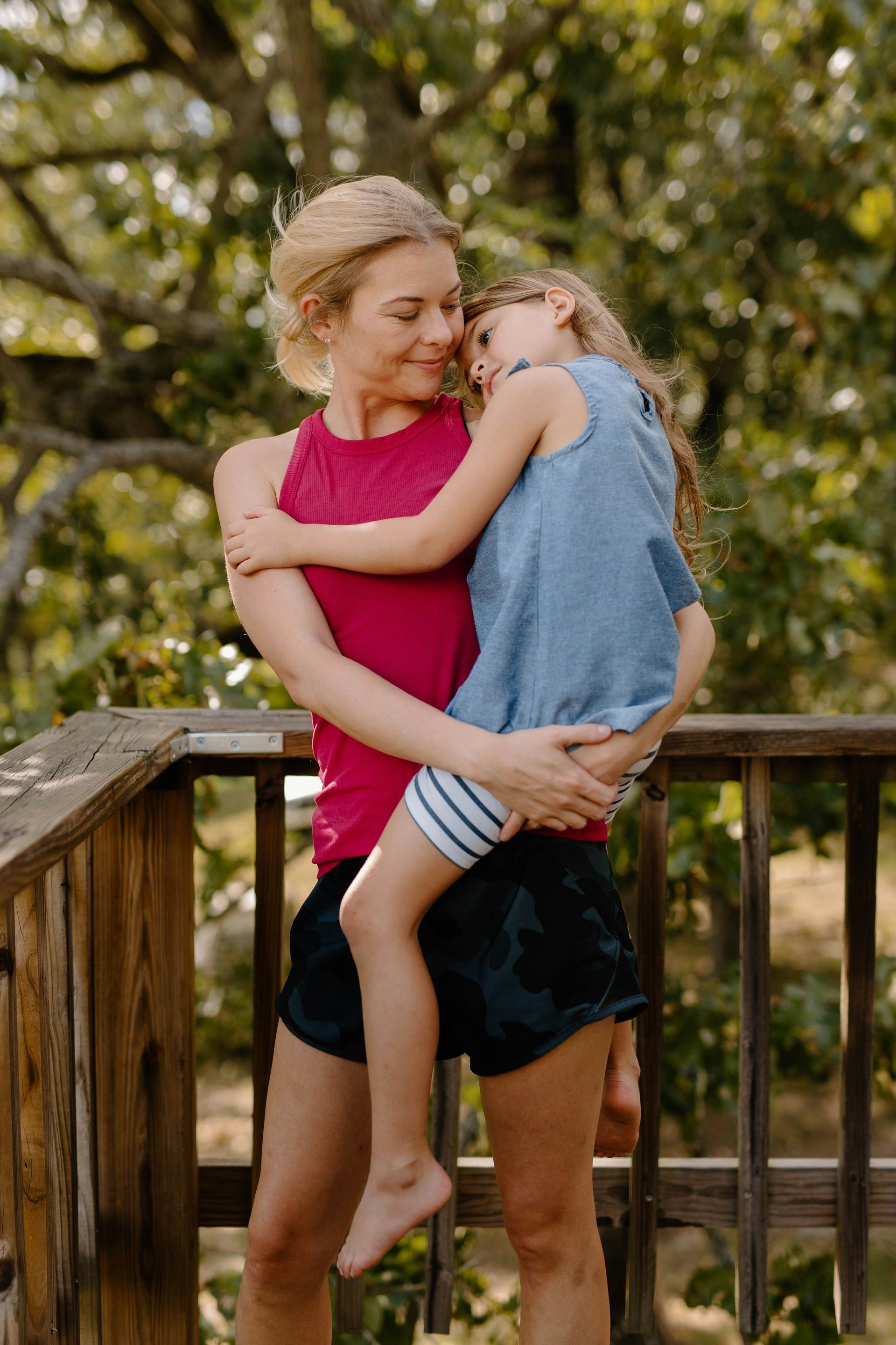 Woman in red top hugging a child. They are on a wooden deck, both looking affectionate.
