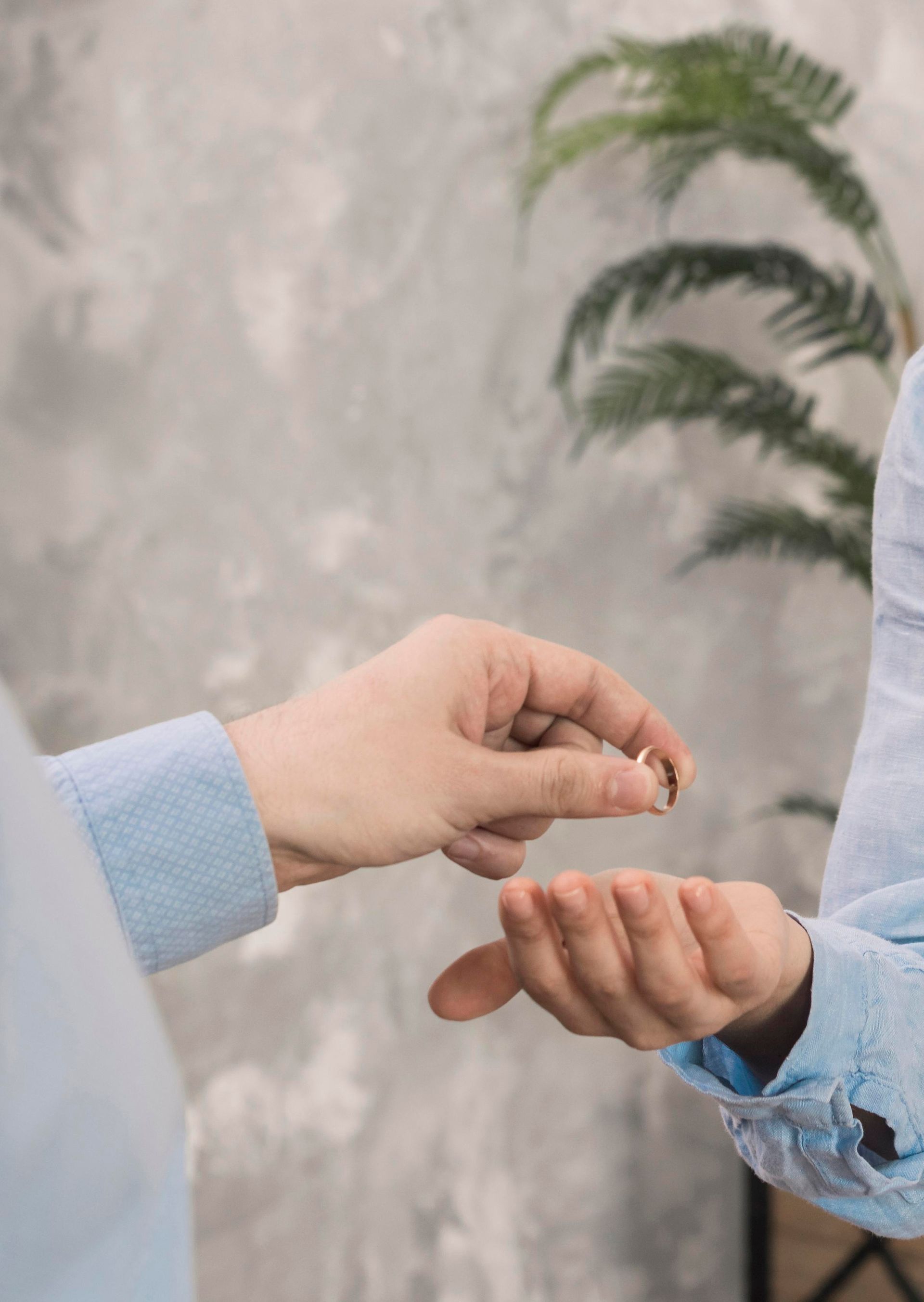 Person handing wedding ring to another, a light blue shirt is visible.