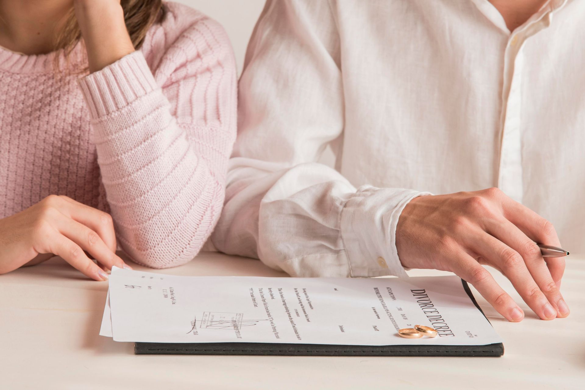 Couple at table with divorce papers, wedding rings, and pens.
