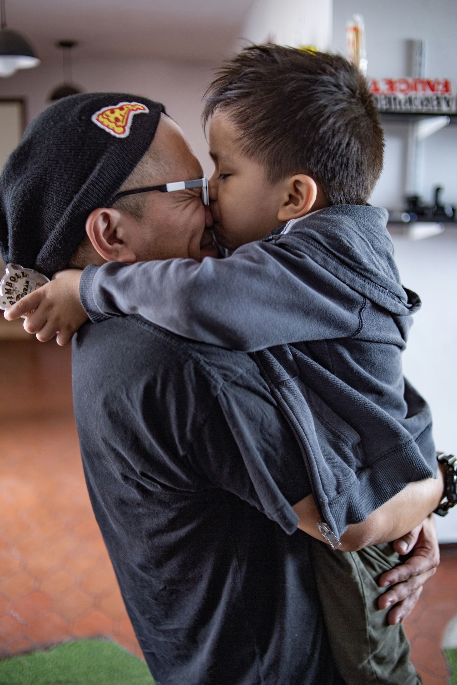 Man holding and kissing a young child; both are smiling, indoors.