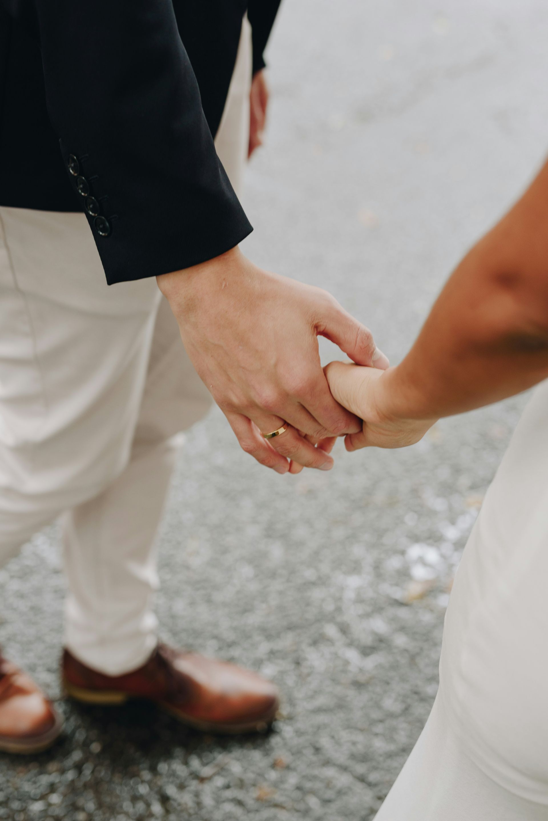 Married couple holding hands, man in tan pants and brown shoes, woman in white dress.