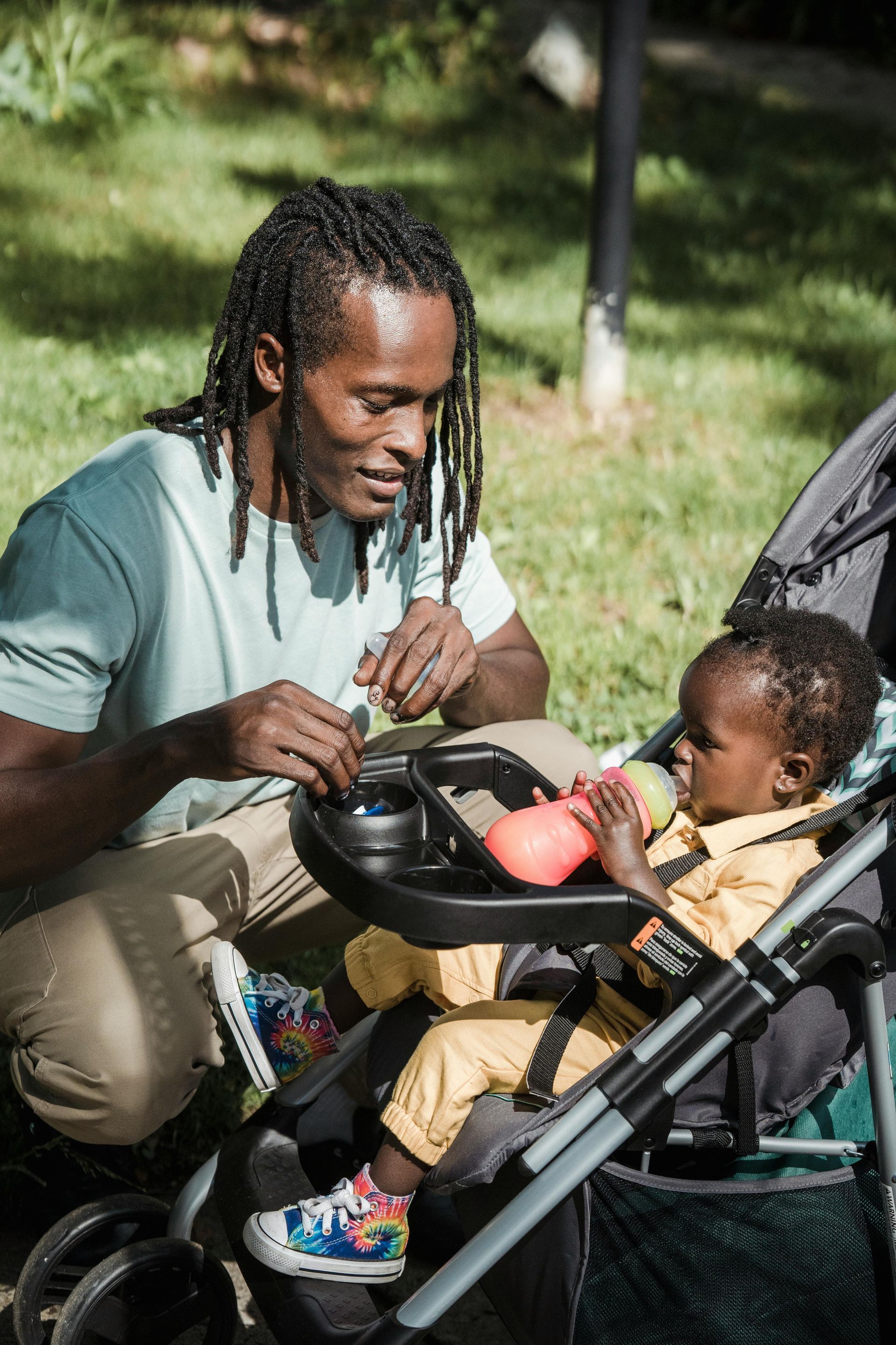 Man in braids tending to baby in stroller, outdoors.
