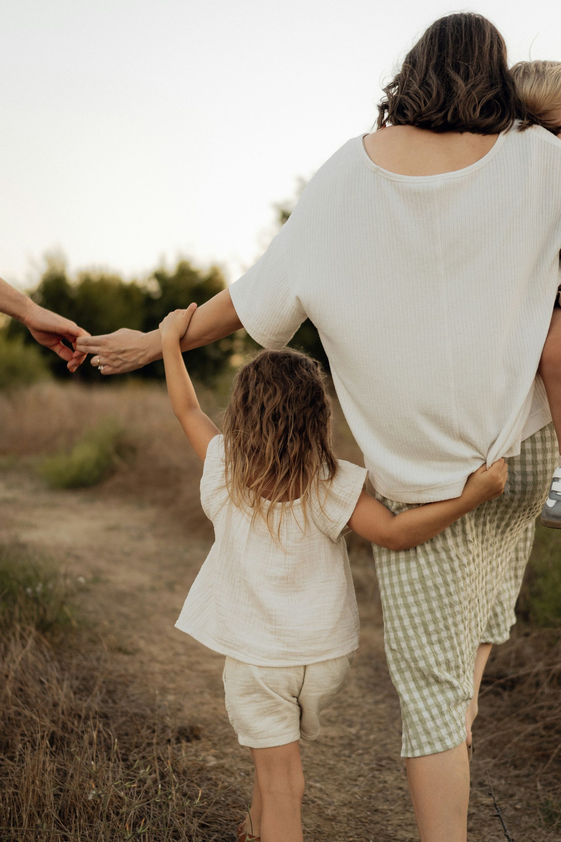 Family walks along a path. Woman carries child, holding hands with another child and adult.